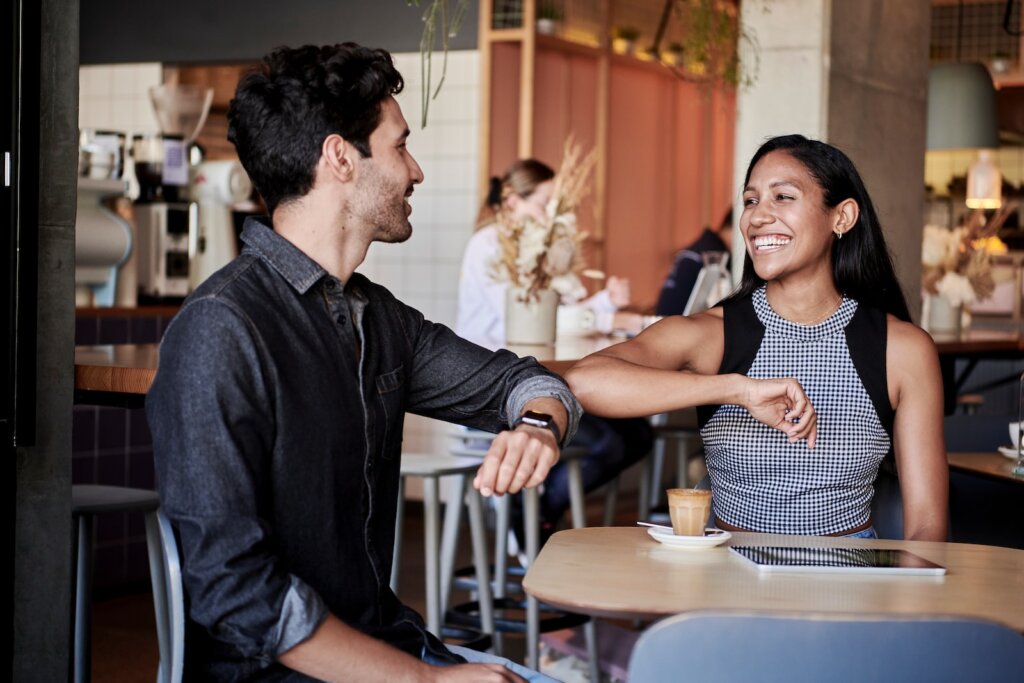 man in black shirt elbow bumping with woman in a restaurant